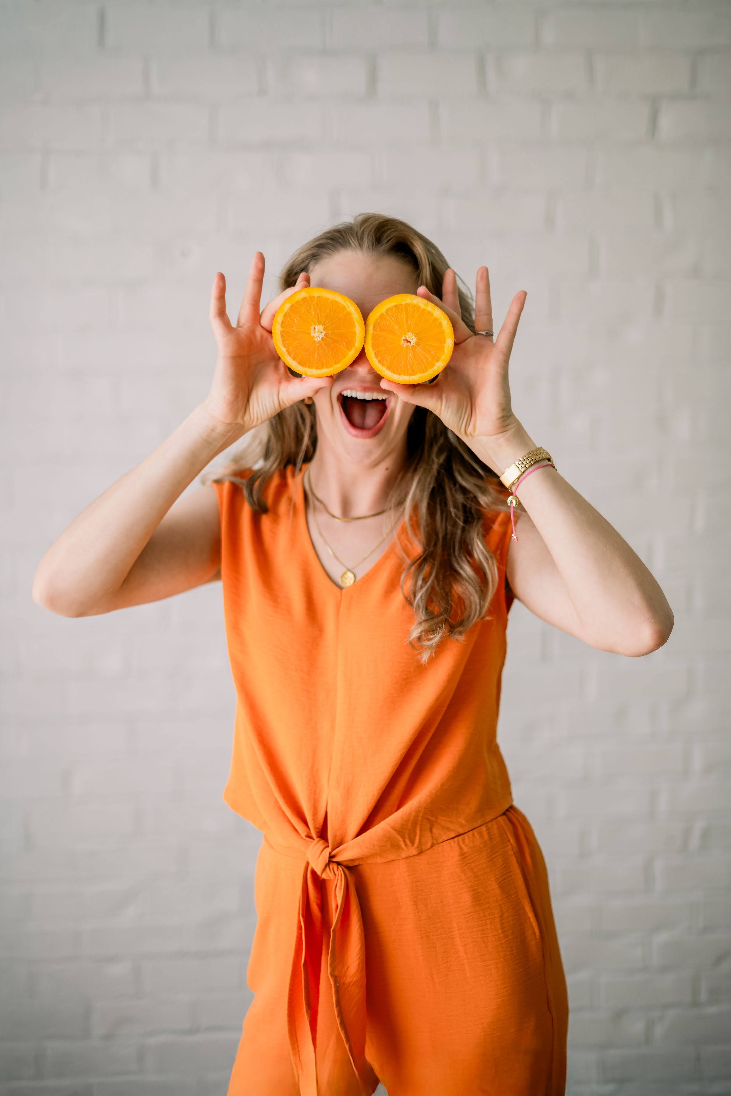 A woman joyfully holding slices of oranges over her eyes
